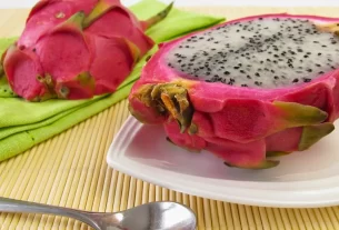 Uma pitaya rosa cortada ao meio, revelando a polpa branca com sementes pretas. A pitaya emagrece e é uma ótima opção para quem busca uma alimentação saudável. Pitaia emagrece?