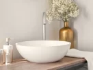 Bancada de banheiro sem reforma, com cuba de apoio branca, acessórios dourados, vaso de flores e toalha clara, mostrando como a decoração pode renovar o ambiente sem obras.