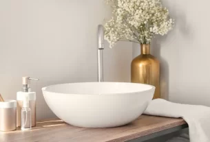 Bancada de banheiro sem reforma, com cuba de apoio branca, acessórios dourados, vaso de flores e toalha clara, mostrando como a decoração pode renovar o ambiente sem obras.