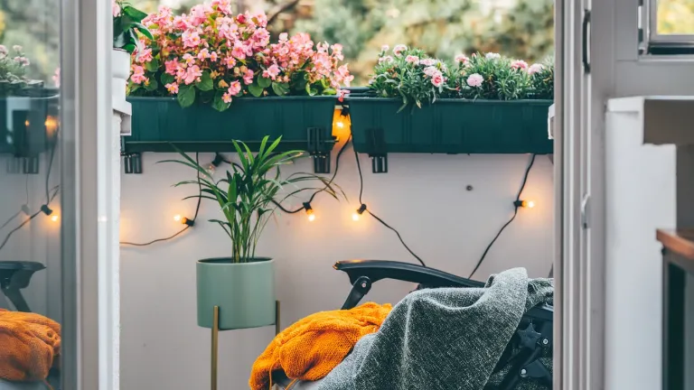Varanda mais charmosa com flores coloridas, luzes decorativas, planta em vaso verde e cadeira com manta cinza e cobertor laranja.